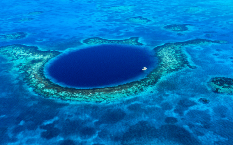 Un círculo de agua azul más oscuro en el océano revela una cueva submarina, rodeada de arrecifes blancos