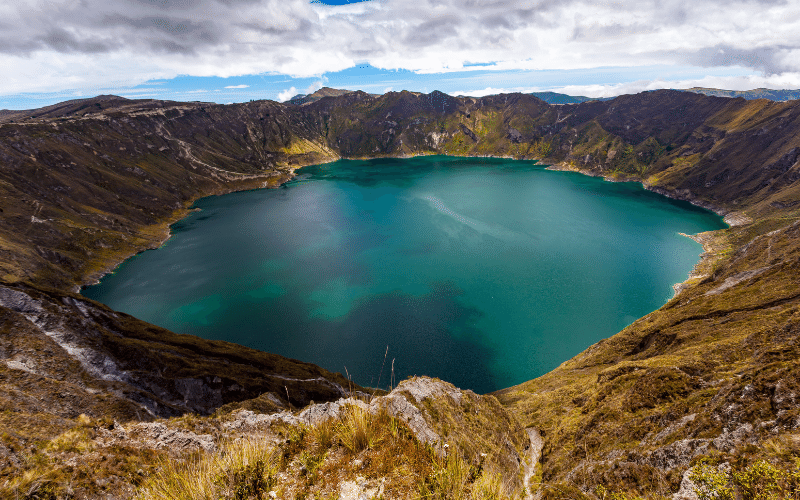 Lago en un cráter rodeado de colinas rocosas en un día nublado, lagos de cráteres